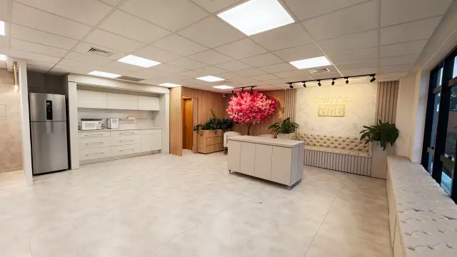 Lounge com copa equipada com geladeira e micro-ondas, balcão central e painel Derma Club ao fundo