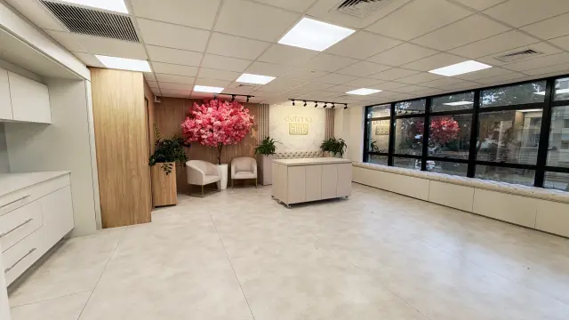 Lounge da Dermalink Academy com árvore de flores rosas, poltronas, balcão central e janelas amplas