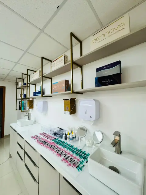 Bancada de apoio da sala de procedimentos com cubas, dispensers, espelhos de mão e prateleiras com produtos