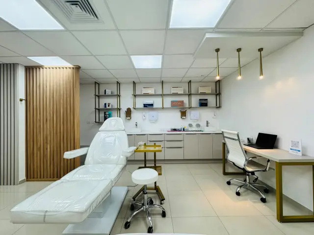 Sala de procedimentos com maca elétrica, bancada com cubas, prateleiras douradas e luminárias pendentes