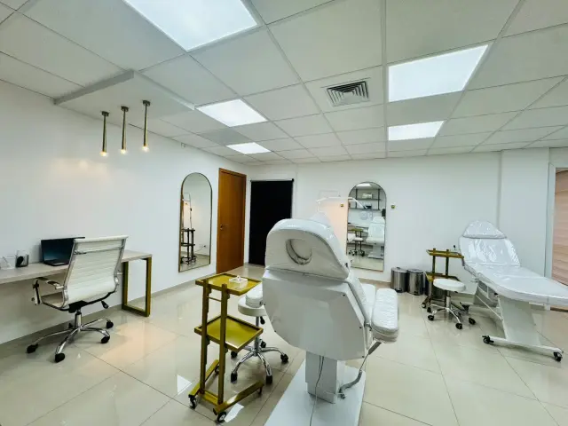 Sala de procedimentos com duas macas, carrinho auxiliar dourado, espelhos em arco e mesa de atendimento