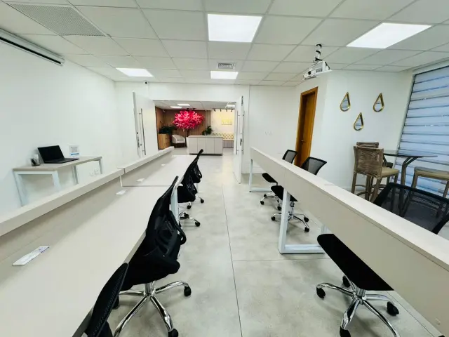 Bancadas paralelas com cadeiras na sala de treinamento e, ao fundo, a passagem para o lounge