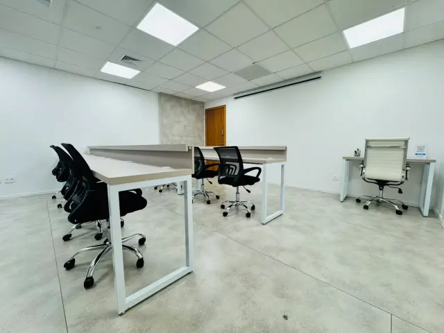Sala de treinamento com mesas brancas, cadeiras pretas e posto do instrutor com cadeira branca
