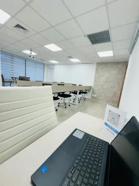 Vista da mesa do instrutor para as bancadas da sala de treinamento, com notebook e display com QR code